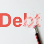 The word "Debt" is printed in large red letters on white paper, with a pencil eraser partially erasing the letters "bt," illustrating the idea of eliminating debt—highlighting why you may need a business tax debt lawyer in 2025.