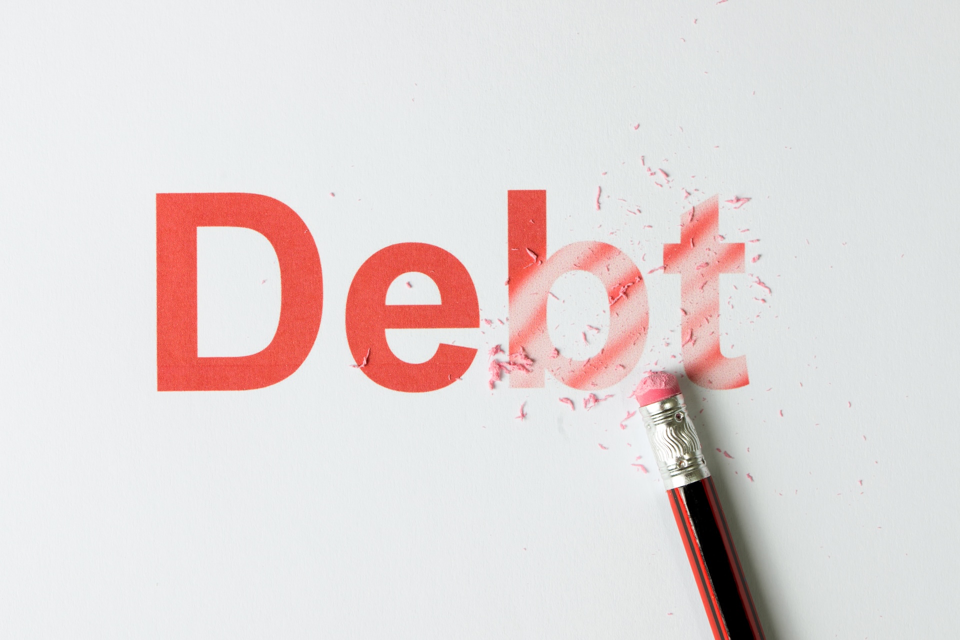 The word "Debt" is printed in large red letters on white paper, with a pencil eraser partially erasing the letters "bt," illustrating the idea of eliminating debt—highlighting why you may need a business tax debt lawyer in 2025.