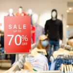 A red sale sign in a clothing store advertises discounts of up to 70% off, much like expert strategies to manage and resolve business tax debt help you save big. Blurred mannequins and clothes on racks appear in the background.