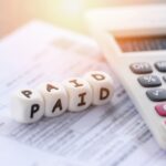 A close-up of a calculator and a document with dice spelling "PAID" placed on top, symbolizing payment or bill settlement—an apt image for Must-Know Taxation Advice for Cryptocurrency Investments.