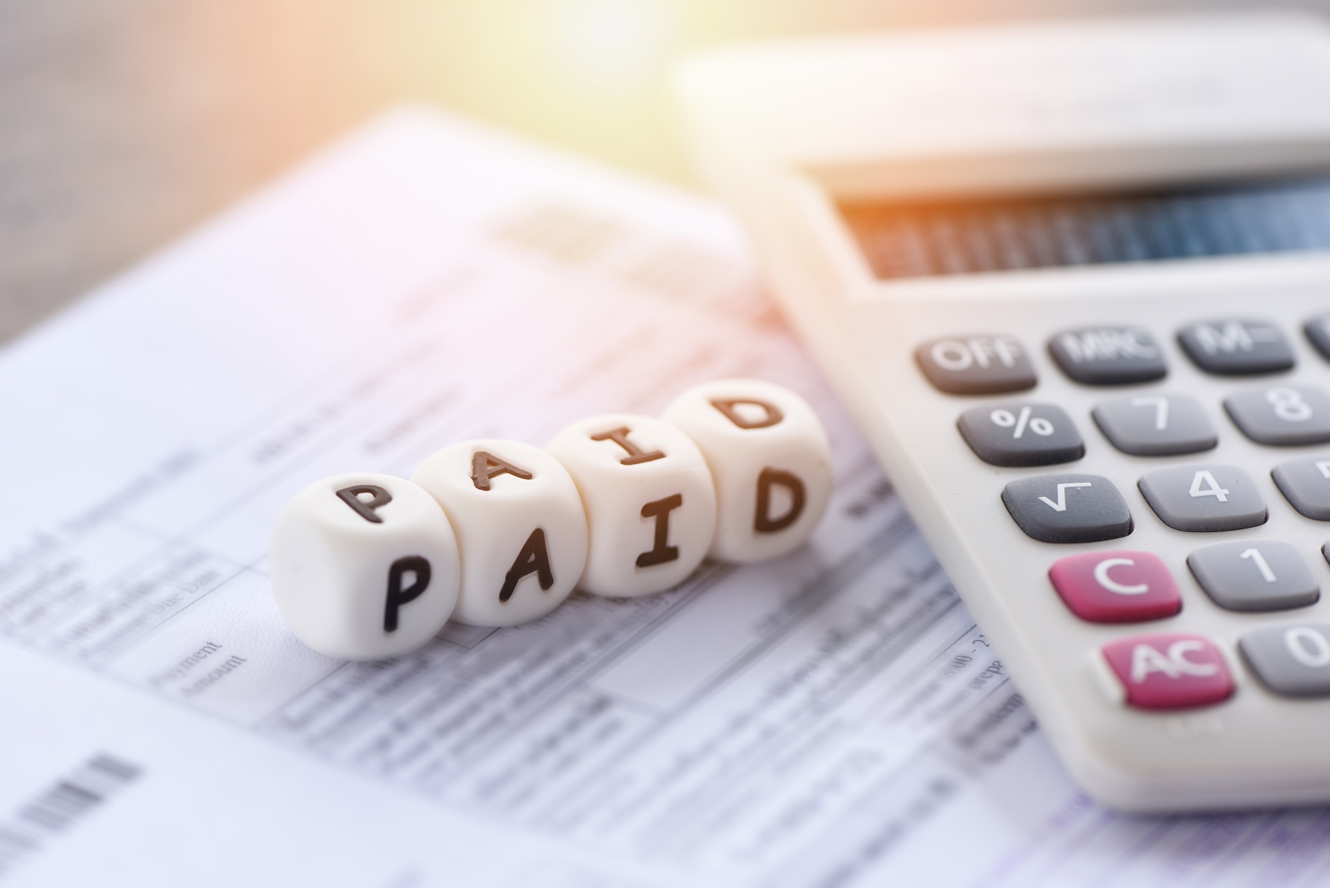 A close-up of a calculator and a document with dice spelling "PAID" placed on top, symbolizing payment or bill settlement—an apt image for Must-Know Taxation Advice for Cryptocurrency Investments.